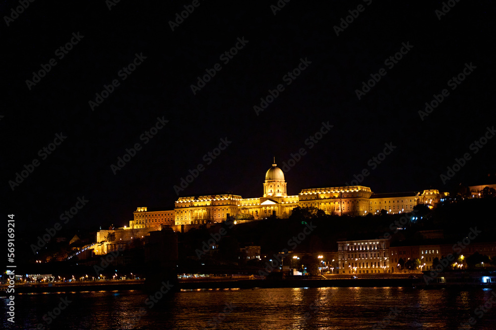 Budapest night landscape with lots of lanterns and illuminated buildings. A pleasure boat is sailing on the river