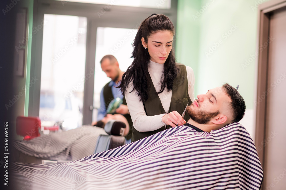 Woman adjusting clients beard with scissors