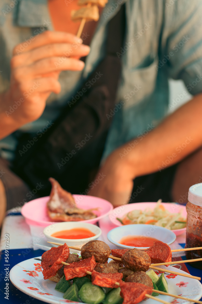 A tourist eating one of the skewers from a plate full of different khmer street food skewers or mhoup taam phlew