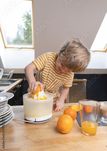 The boy squeezes orange juice in the kitchen by himself photo