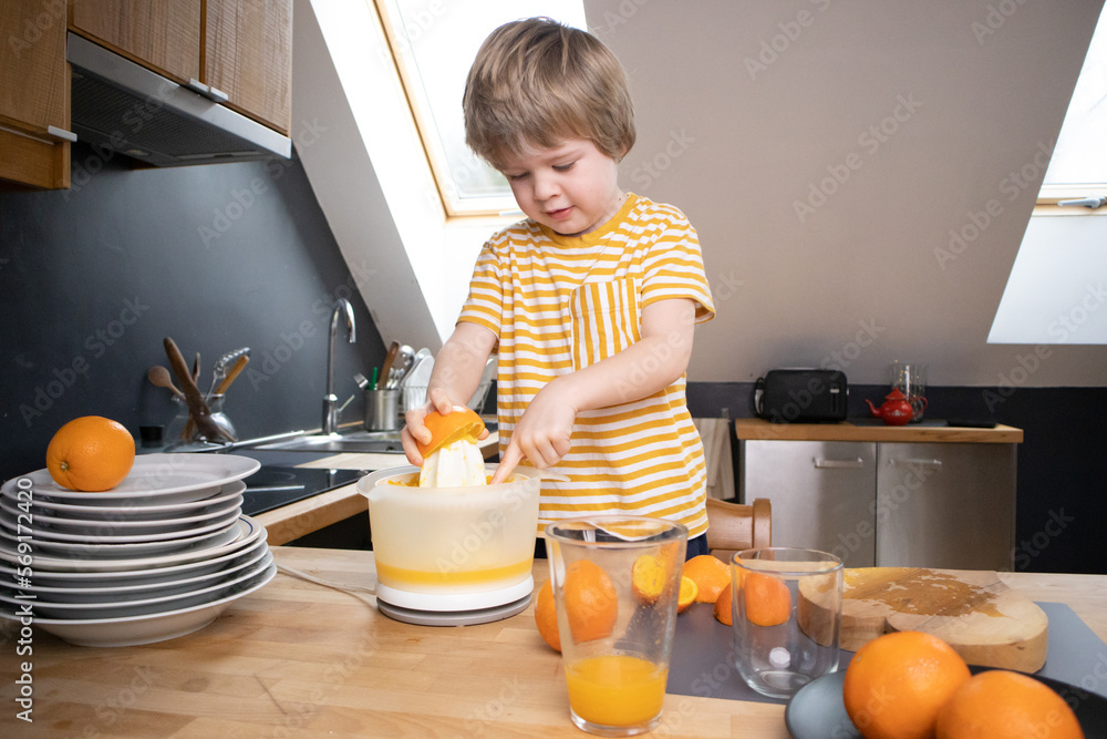 The boy squeezes orange juice in the kitchen by himself The boy squeezes orange juice in the kitchen by himself