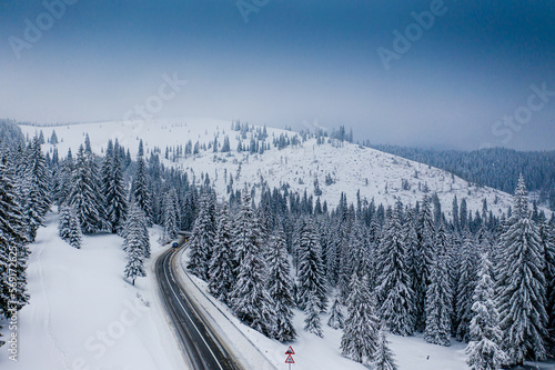 Amazing winter road through a forest covered with snow, aerial view over a beautiful landscape.