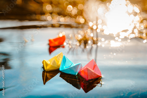 Multicolored paper boats. Colorful pink yellow blue orange ships in big spring snow puddle on winter street. Warm wet rainy weather, old grass. Hello spring, autumn. Children play, have fun outdoors photo