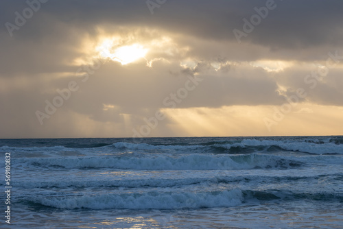Foamy sea waves and sun peaking through the clouds at early evening