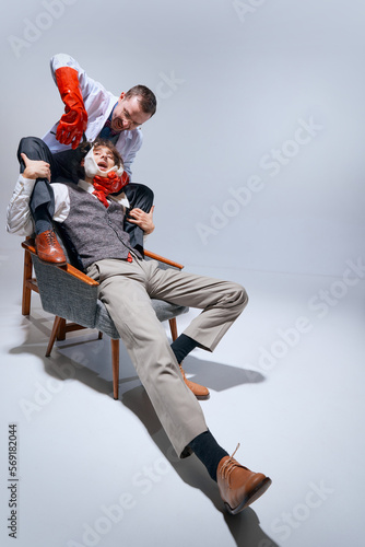 Fototapeta Naklejka Na Ścianę i Meble -  Young scared man sitting on chair, visiting dentist. Crazy insane dentist holding man's face and pulling his teeth against grey studio background. Concept of profession, occupation, medicine, emotions