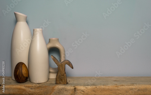 Rustic wooden decor white vases and an easter bunny figure on a wooden shelf. Copy space.