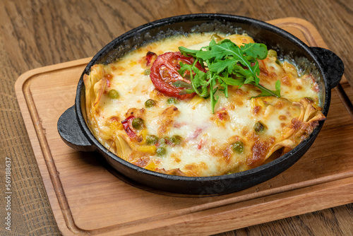 Lasagna sprinkled with greens and tomatoes in a pan on a board