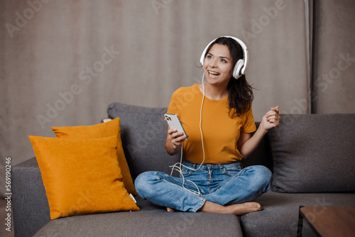 Happy indian or arabian girl resting on cozy sofa at home, listening to music