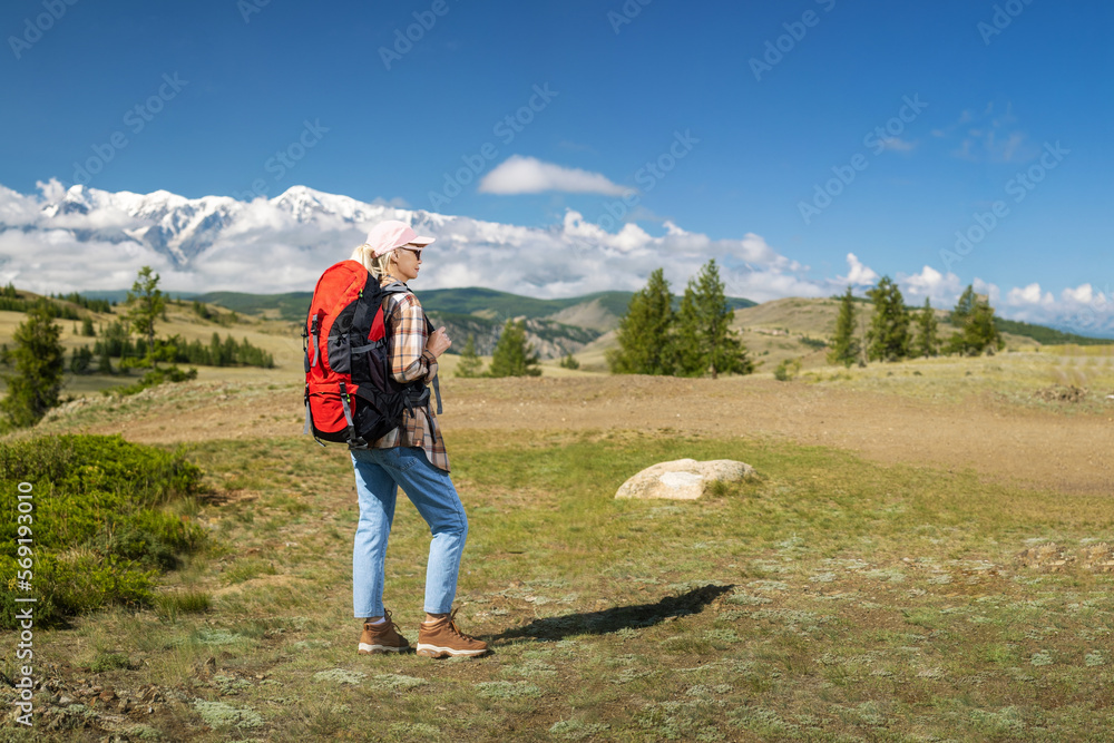 Naklejka premium Woman traveler with backpack hiking in mountains with beautiful summer landscape on background. Travel, summer vacation and healthy lifestyle concept.