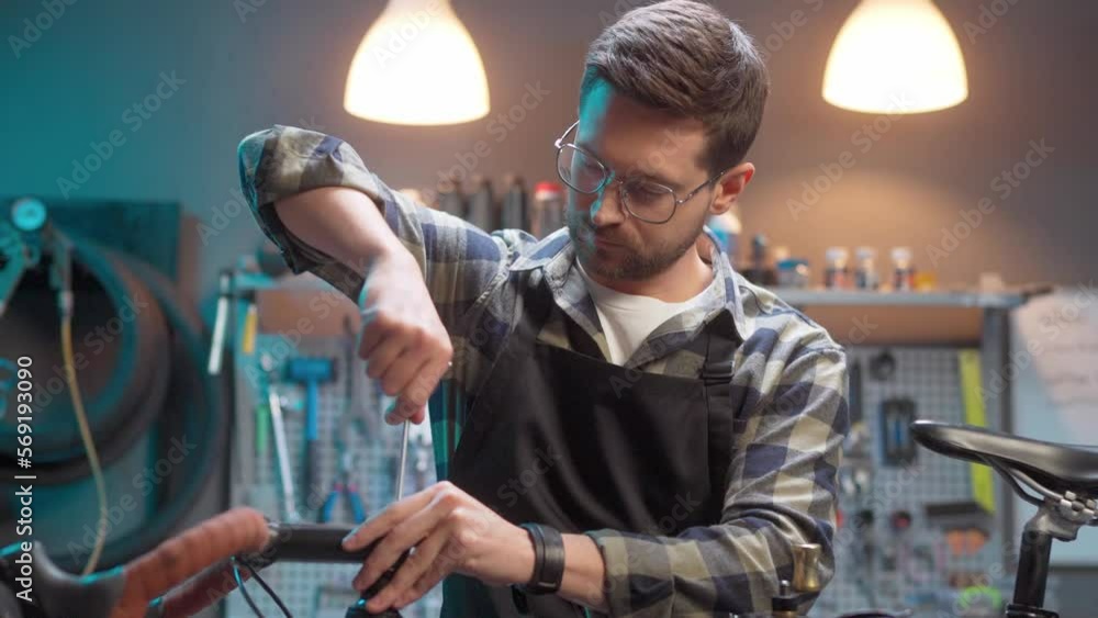 Beautiful busy focused caucasian man fixing bike with screwdriver at authentic garage. Attractive male craftsman doing hobby repairing bicycle with tools wearing glasses. Beautiful busy focused caucasian man fixing bike with screwdriver at authentic garage. Attractive male craftsman doing hobby repairing bicycle with tools wearing glasses.