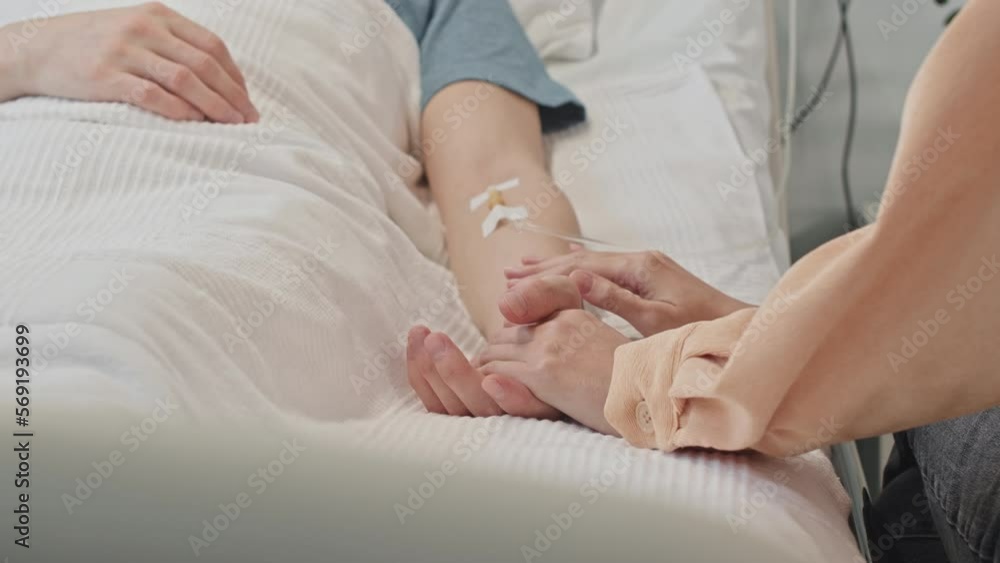 Cropped shot of wife supporting husband lying on bed in hospital ward with iv drip Cropped shot of wife supporting husband lying on bed in hospital ward with iv drip