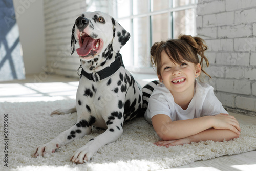 Home portrait of a girl hugging with a Dalmatian dog on a carpet at home.