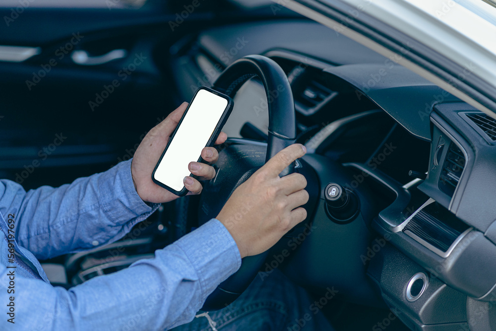 Male hand holding a smartphone with a white mockup on the screen. car steering wheel background Young man showing phone screen sitting in the driver's seat The app driver calls the user.