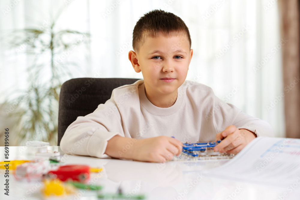Portrait of child boy plays with an electronic constructor at home at the desk. Future engineer learns to assemble electronic circuits Portrait of child boy plays with an electronic constructor at home at the desk. Future engineer learns to assemble electronic circuits