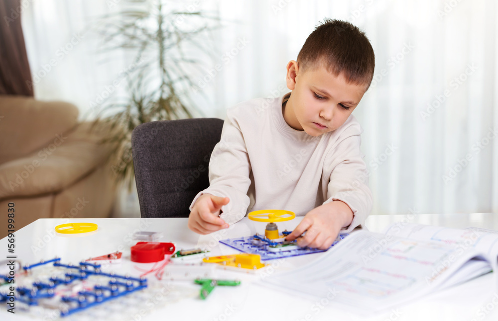 School kid boy plays with an electronic constructor at home at the table. Future engineer learns to assemble electronic circuits. Creative hobby. New skills School kid boy plays with an electronic constructor at home at the table. Future engineer learns to assemble electronic circuits. Creative hobby. New skills