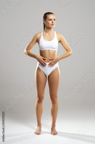 Young, fit and beautiful blond woman in white swimsuit isolated on grey background. Healthcare, diet, sport and fitness concept.