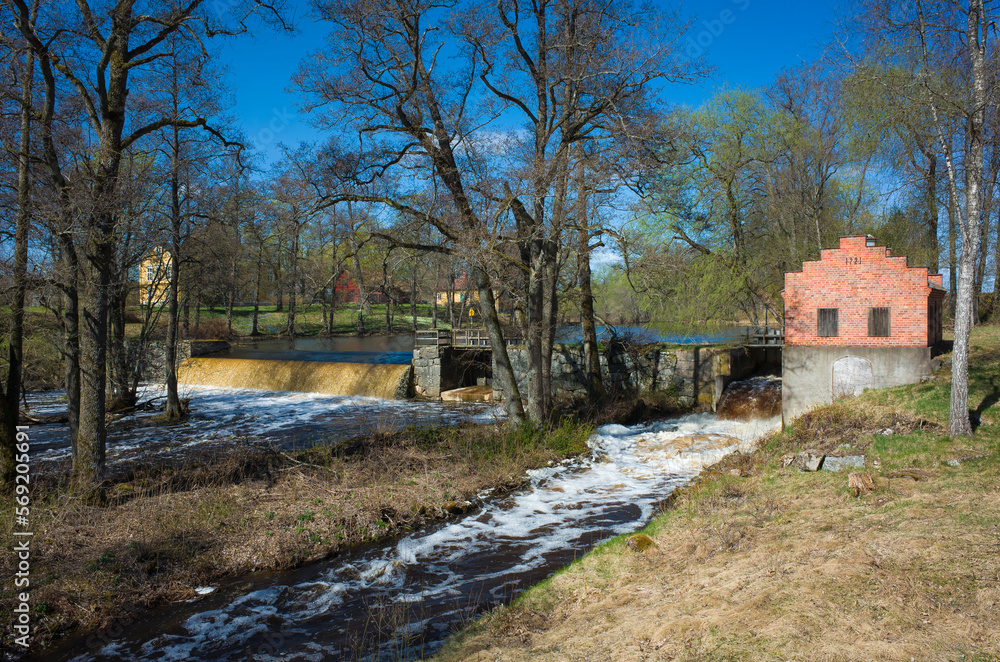 Small hydroelectric dam on Svartan river in Skerike with old red brick Turbine house, Spring nature in Sweden