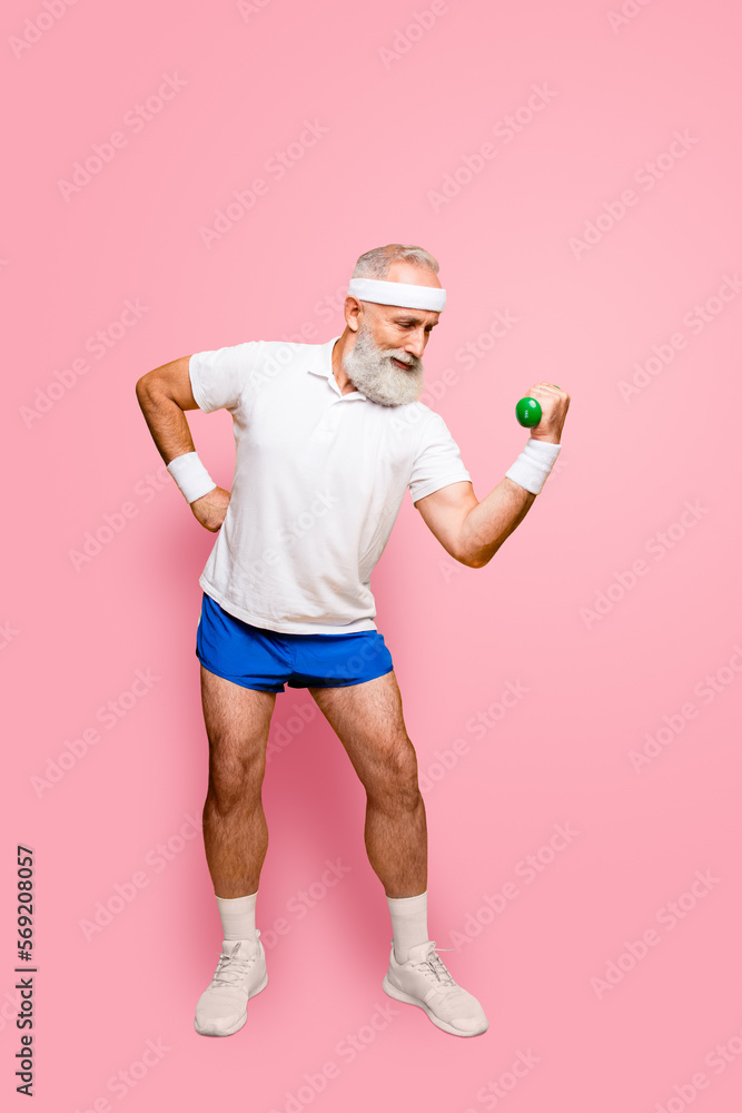 Fototapeta premium Cool grandpa with confident grimace exercising holding equipment up, lifts it with strength and power, wearing blue sexy shorts. Body care, hobby, weight loss, lifestyle