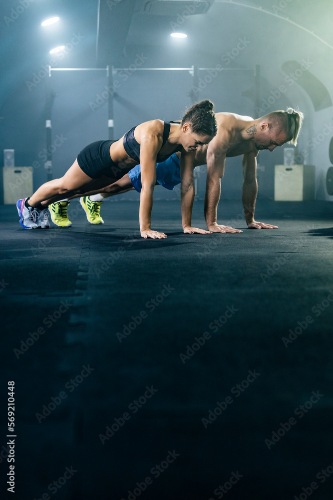 Fototapeta premium Muscular man and woman in sportswear doing push up in gym.