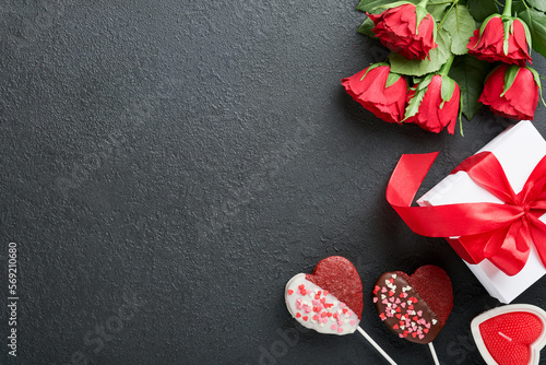 Fototapeta Naklejka Na Ścianę i Meble -  Valentines day card. Rose red flowers brownie cookies and chocolate candy on heart shaped, gift box with wine on black background. Mothers or Womens Day greeting card. Top view flat lay