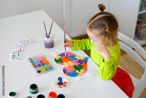 A three-year-old girl draws a drawing for children suffering from autism with a picture of a heart from puzzles. Learn to be tolerant from childhood