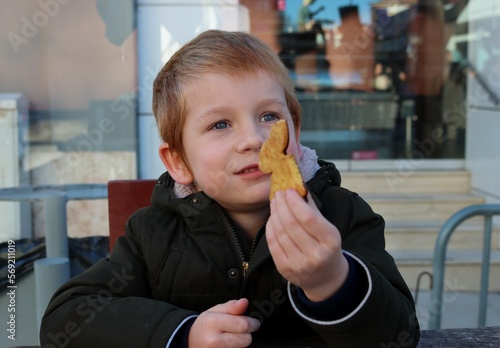The blond boy holds a cookie in his hand and looks into the distance with a smile. Happy five year old boy.