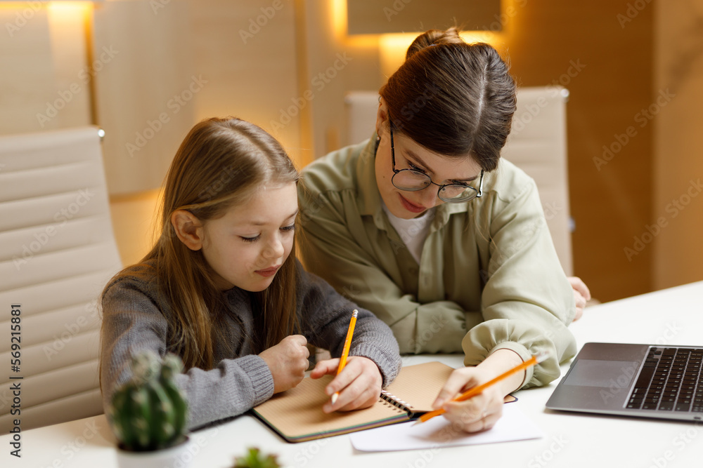 Private teacher for a child, individual lesson with a tutor. Mom and daughter do homework at the table. Private teacher for a child, individual lesson with a tutor. Mom and daughter do homework at the table.