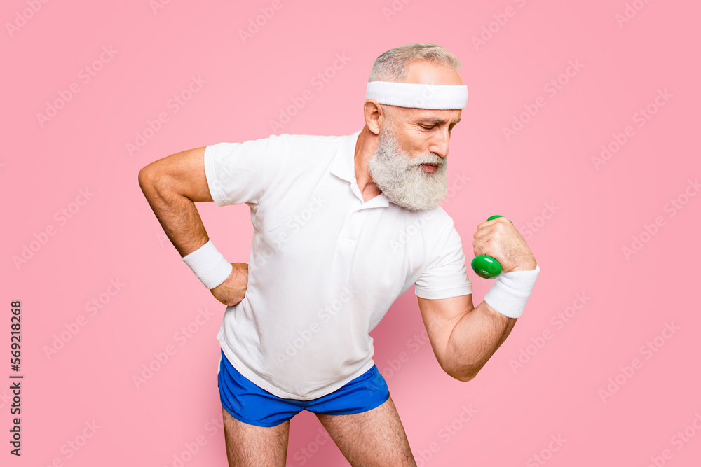Naklejka premium Body care, hobby, weight loss lifestyle. Cool grandpa with confident grimace exercising holding equipment up, lifts it with strength and power, wearing blue sexy shorts, show legs