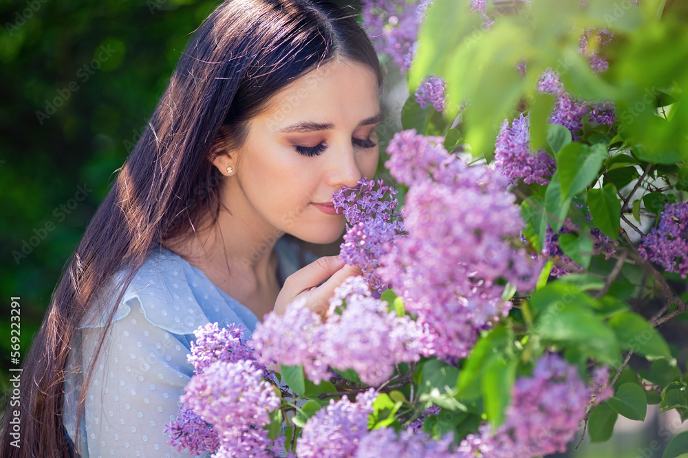 Beautiful brunette girl, with long hair, smells lilac flowers, in the summer in the park, sunny day Beautiful brunette girl, with long hair, smells lilac flowers, in the summer in the park, sunny day