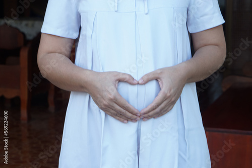Closeup 6 month pragnant woman wears white dress, hands touch her big belly. Concept, pragnancy, motherhood. Health care. 