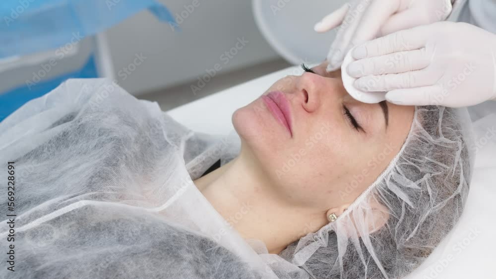 Cosmetologist is applying cream with anesthesia on patient's face skin before biorevitalization procedure. Woman in beauty clinic with doctor beautician preparing to treatment using numbing cream. Cosmetologist is applying cream with anesthesia on patient's face skin before biorevitalization procedure. Woman in beauty clinic with doctor beautician preparing to treatment using numbing cream.