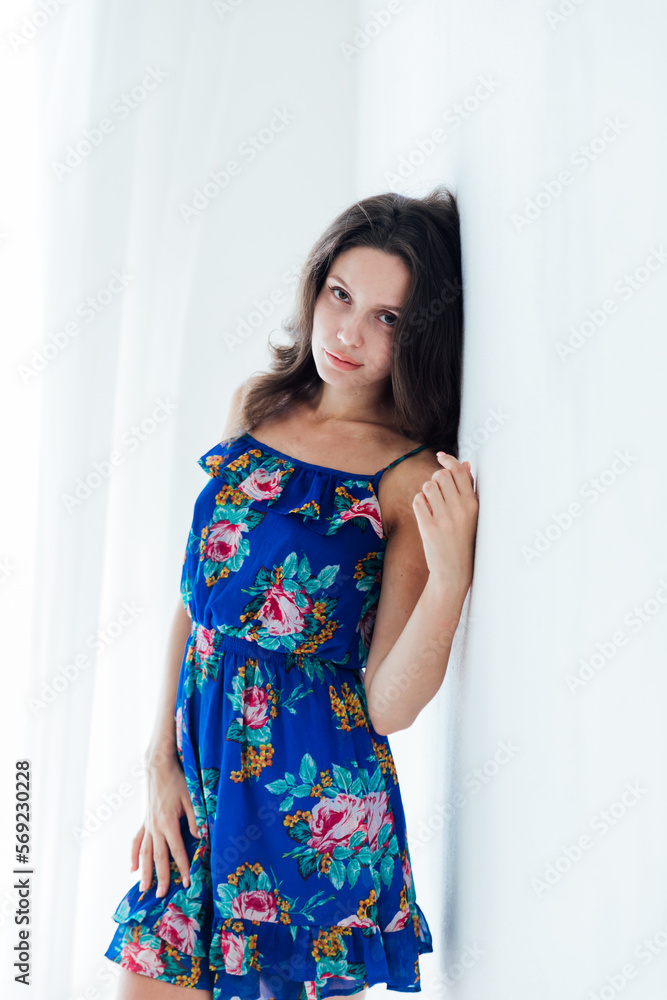 brunette woman in a blue floral dress against a white wall brunette woman in a blue floral dress against a white wall