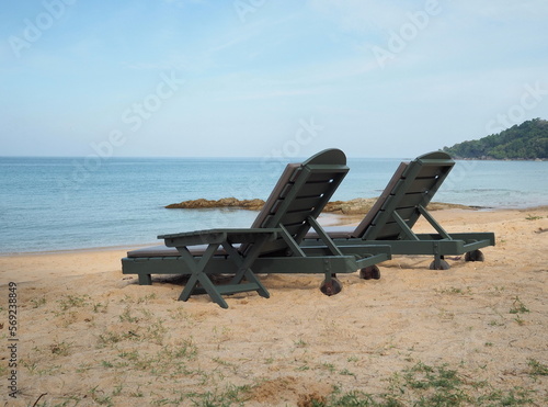 Black beach chairs with brown cushions are located on the beach for tourists to sit and relax while waiting to swim or watch the sea. 2 lounge chairs on the sandy beach near the sea. 