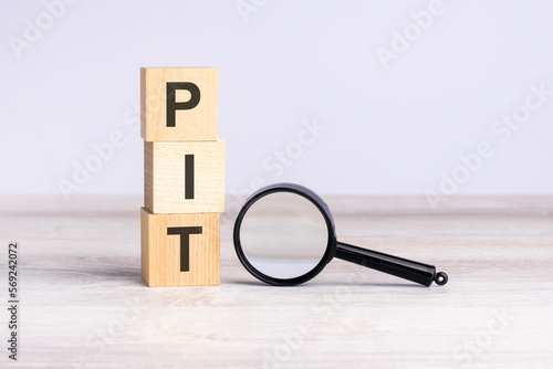 PIT - personal income tax - text wooden cube blocks and magnifying glass on table. strategy, marketing, and content concept