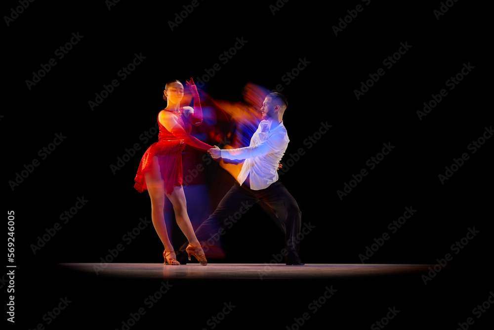 Beautiful young people, man and woman dancing tango, ballroom over black background with mixed neon lights. Concept of hobby, lifestyle, action, beauty of movements, emotions, fashion, art