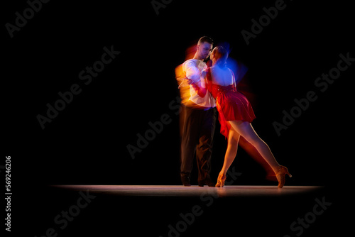 Fototapeta Naklejka Na Ścianę i Meble -  Man and woman, professional dancers in stylish stage costumes performing ballroom, tango over black background with mixed neon lights. Concept of hobby, lifestyle, action, beauty of movements, art