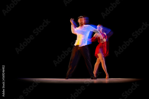 Dynamic movements. Young man and woman dancing tango, ballroom over black background with mixed neon lights. Concept of hobby, lifestyle, action, beauty of movements, emotions, fashion, art