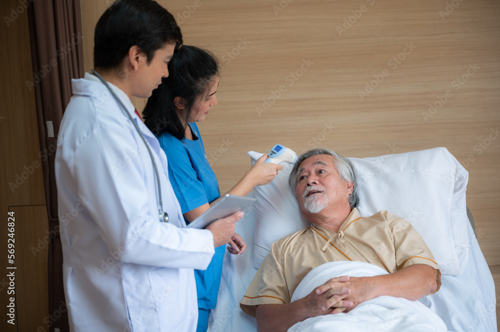 Obraz premium Smiling senior male patient lying and sitting on bed resting while nurse and doctor in lab coat and stethoscope showing digital tablet screen to man in a hospital room