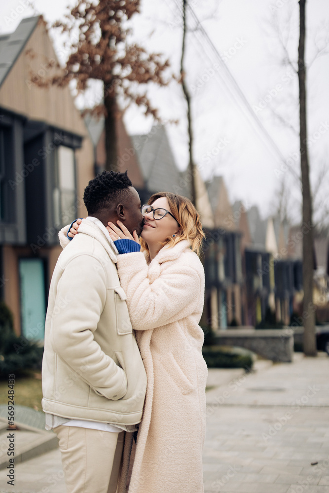Young interracial couple embraces on street against background of houses. Young interracial couple embraces on street against background of houses.