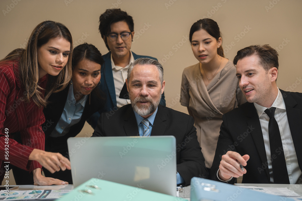 Senior and successful business man sitting with team and colleagues in formal clothing cheering and getting excited over confirmation of deal and enjoying the profits while using laptop Senior and successful business man sitting with team and colleagues in formal clothing cheering and getting excited over confirmation of deal and enjoying the profits while using laptop