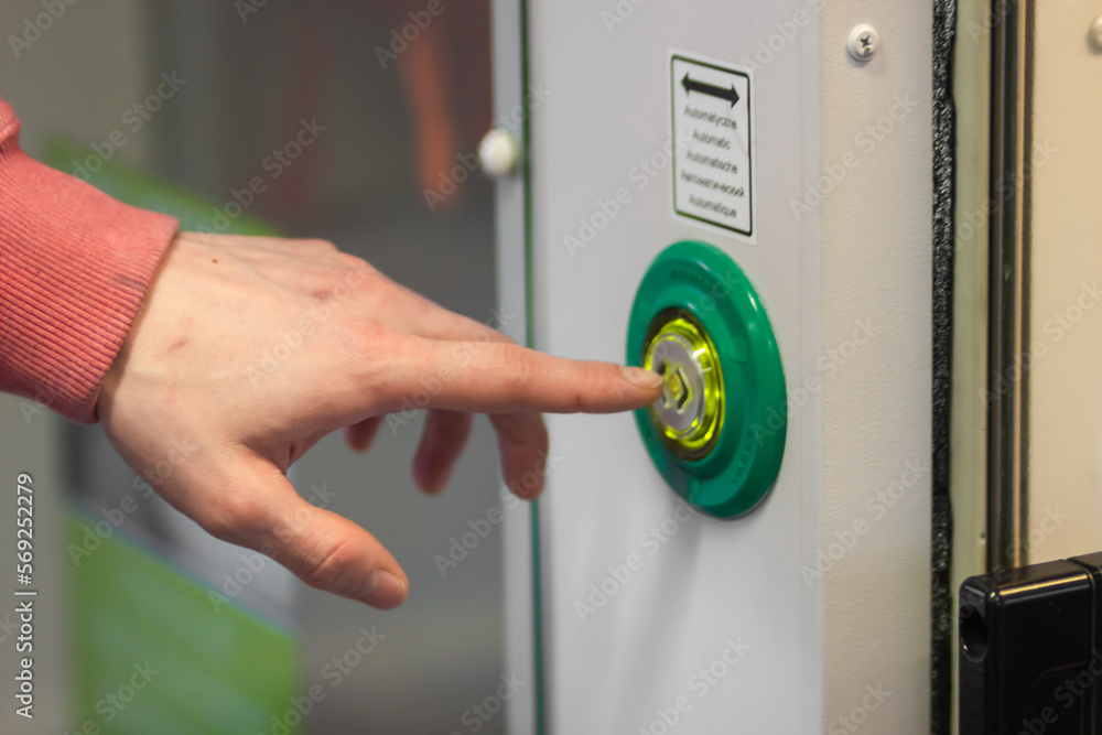 Man's hand index finger presses the door control green button to open doors in a modern electric train or subway car.