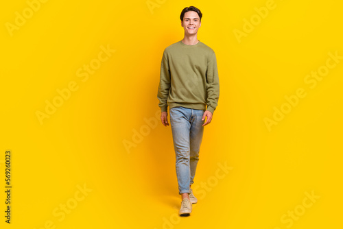Full size portrait of cheerful young person walking good mood empty space isolated on yellow color background