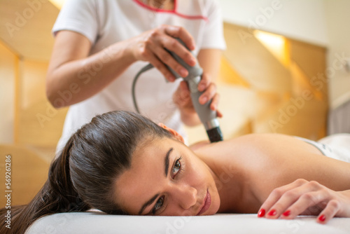 Extracorporeal shockwave therapy in beauty salon. Physical therapy for neck and back muscles spine with shock waves. Young woman wearing protective mask during treatment in salon. Close up.