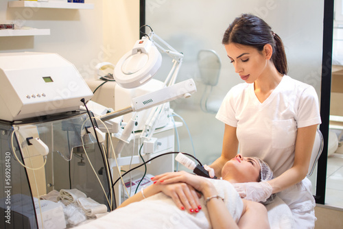 Doctor with Ultrasonic scraber doing procedure of ultrasonic cleaning of female client neck at beauty salon. photo