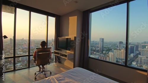 Bild auf Leinwand The man sits on an chair enjoys view of sunset of big city in his apartment on high floor of skyscraper