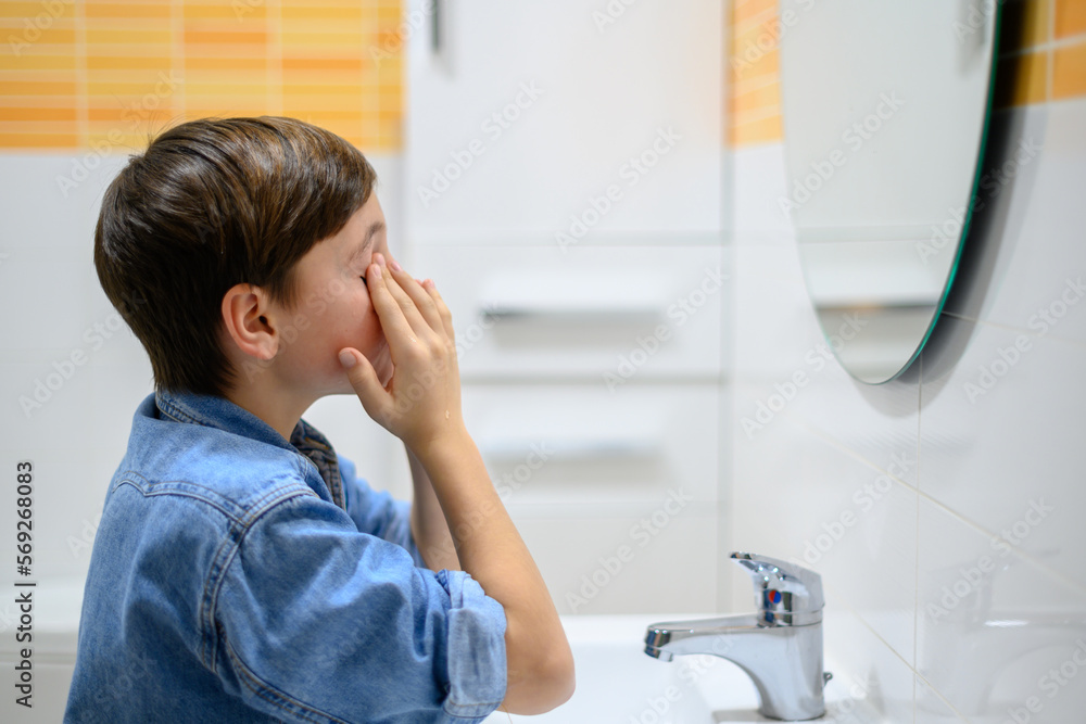 Boy washes his face in front of the mirror in his bathroom.