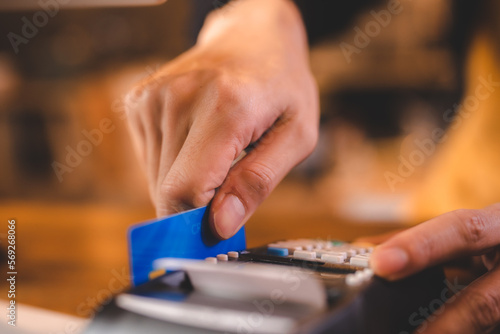 Closeup of hands of a young female cashier at barista swiping bank debit and credit card on NFC technology machine while processing payment for beverage and food ordered by customer