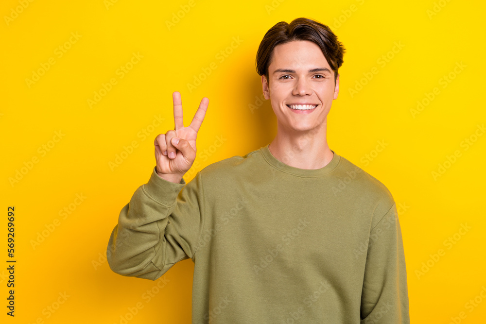 Portrait of cheerful young man beaming smile arm fingers demonstrate v-sign isolated on yellow color background Portrait of cheerful young man beaming smile arm fingers demonstrate v-sign isolated on yellow color background