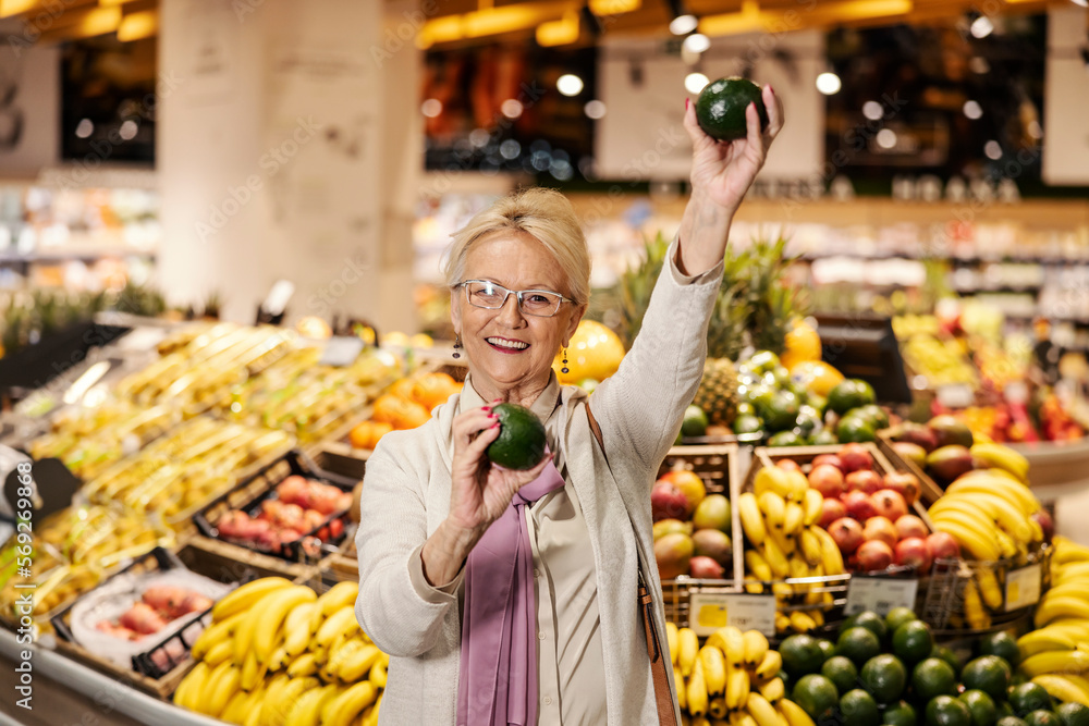 A happy senior woman is dancing with avocado in supermarket. A happy senior woman is dancing with avocado in supermarket.
