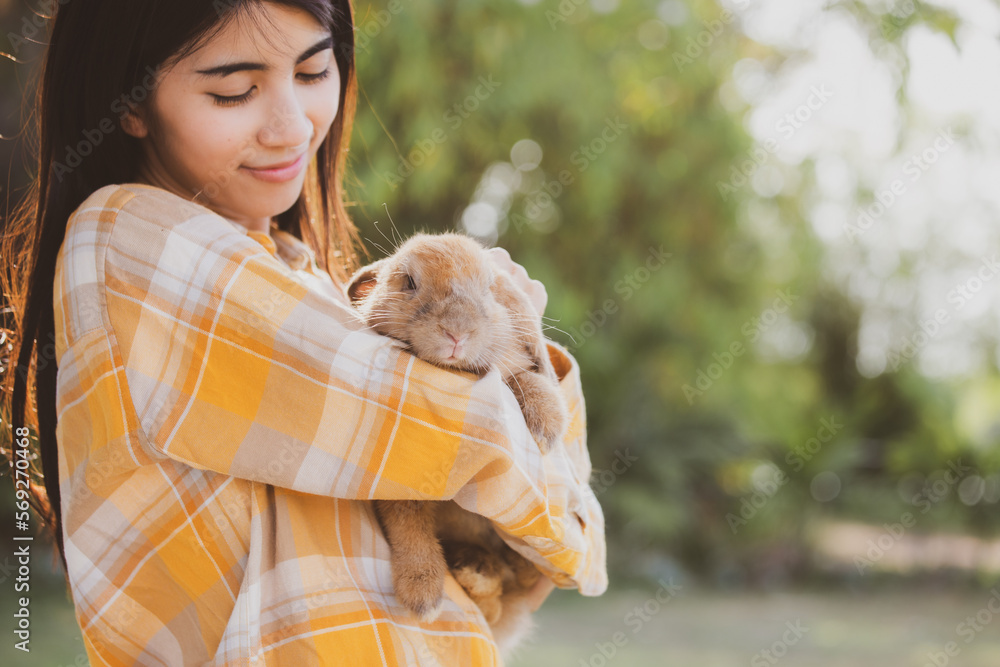 Young smiling and innocent girl holding and hugging a cute little rabbit with closed eyes and caressing her on back Young smiling and innocent girl holding and hugging a cute little rabbit with closed eyes and caressing her on back